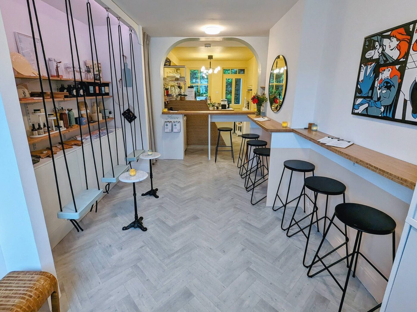 The long narrow room, with shelves and swing seats on the left, stools along a bamboo counter on the right and a yellow back room through an arch.