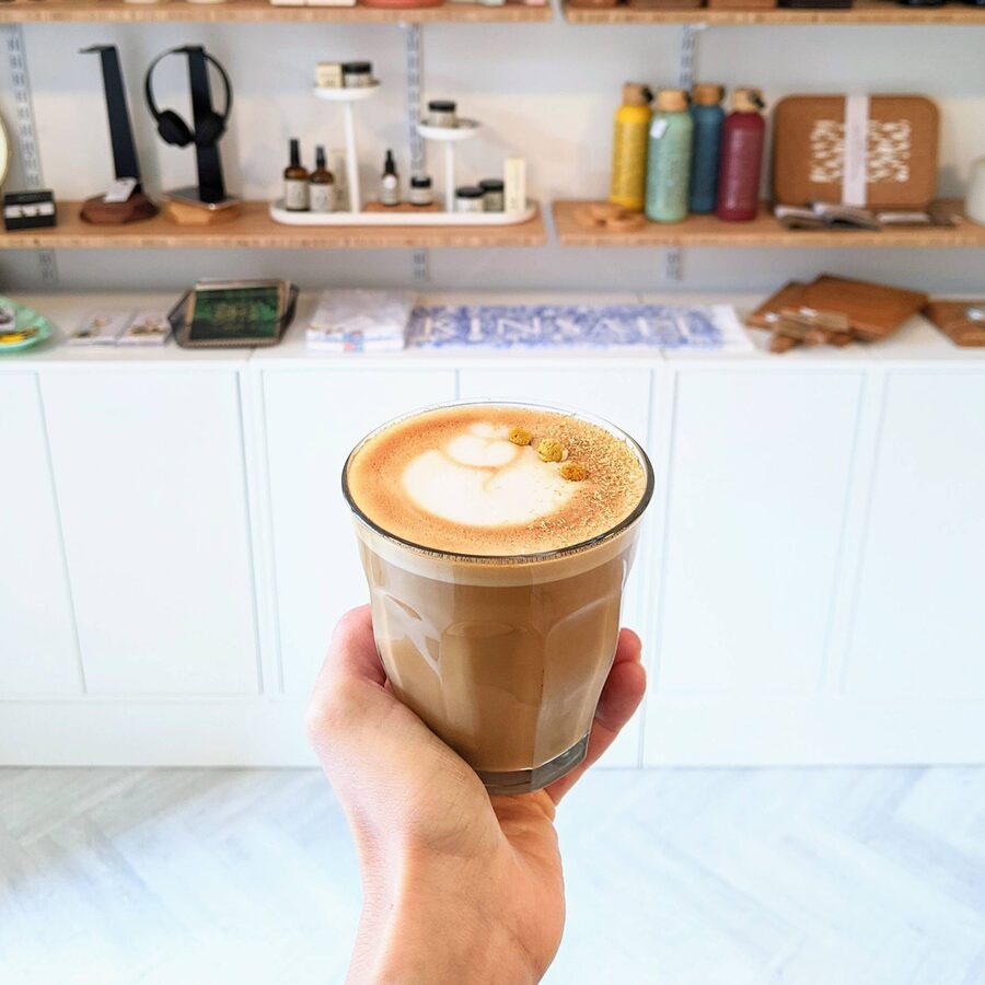 A hand holding a latte in a glass in front of the retail shelves.
