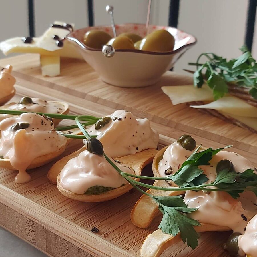 A bamboo board of small bites with a bowl of olives and slices of cheese.