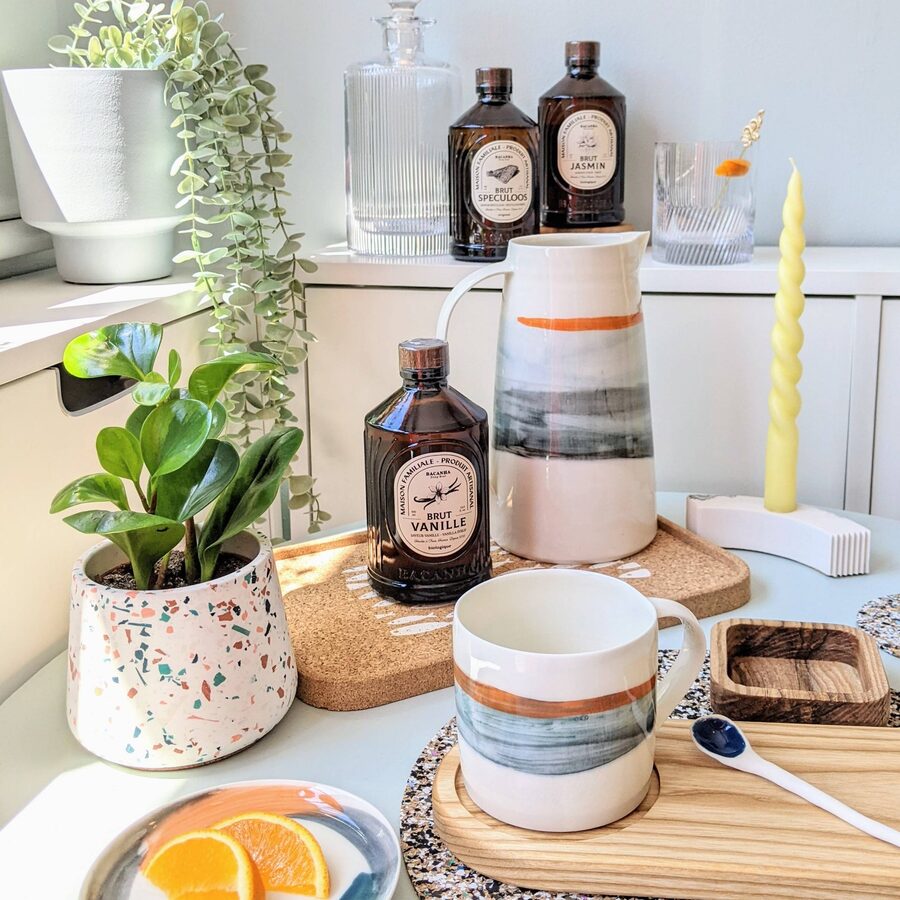 Syrup bottles, a striped ceramic jug and mug, a plant and a yellow candle on a shelf.