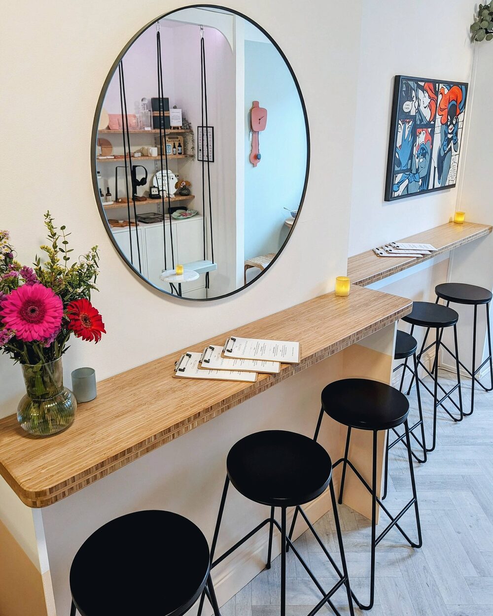A bamboo counter with black stools, a round mirror, a vase of flowers and menus on clipboards.